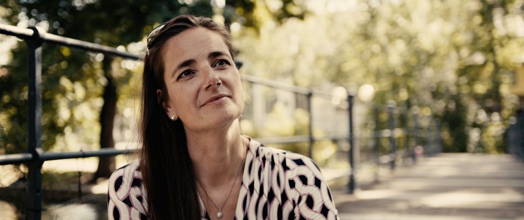 Annelie lächelt und blickt zur Seite, im Hintergrund ein Park mit Brücke