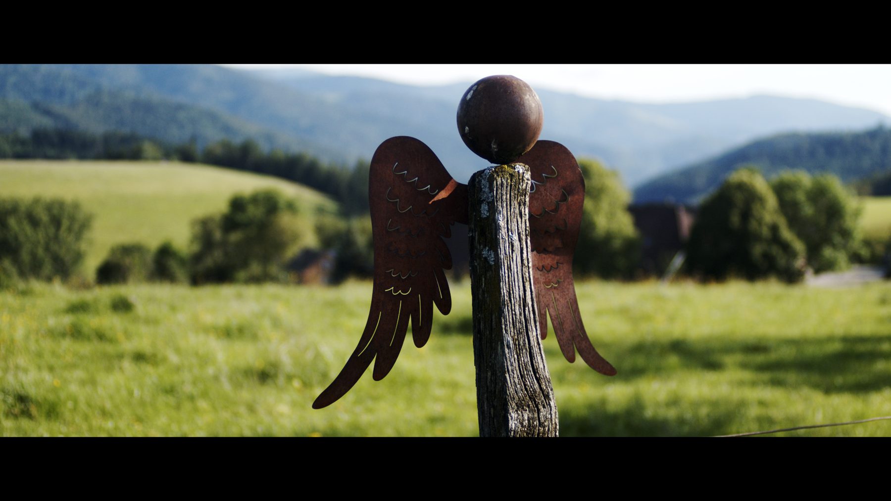 Engelsflügel-Skulptur auf einem Holzpfahl vor grüner Hügellandschaft