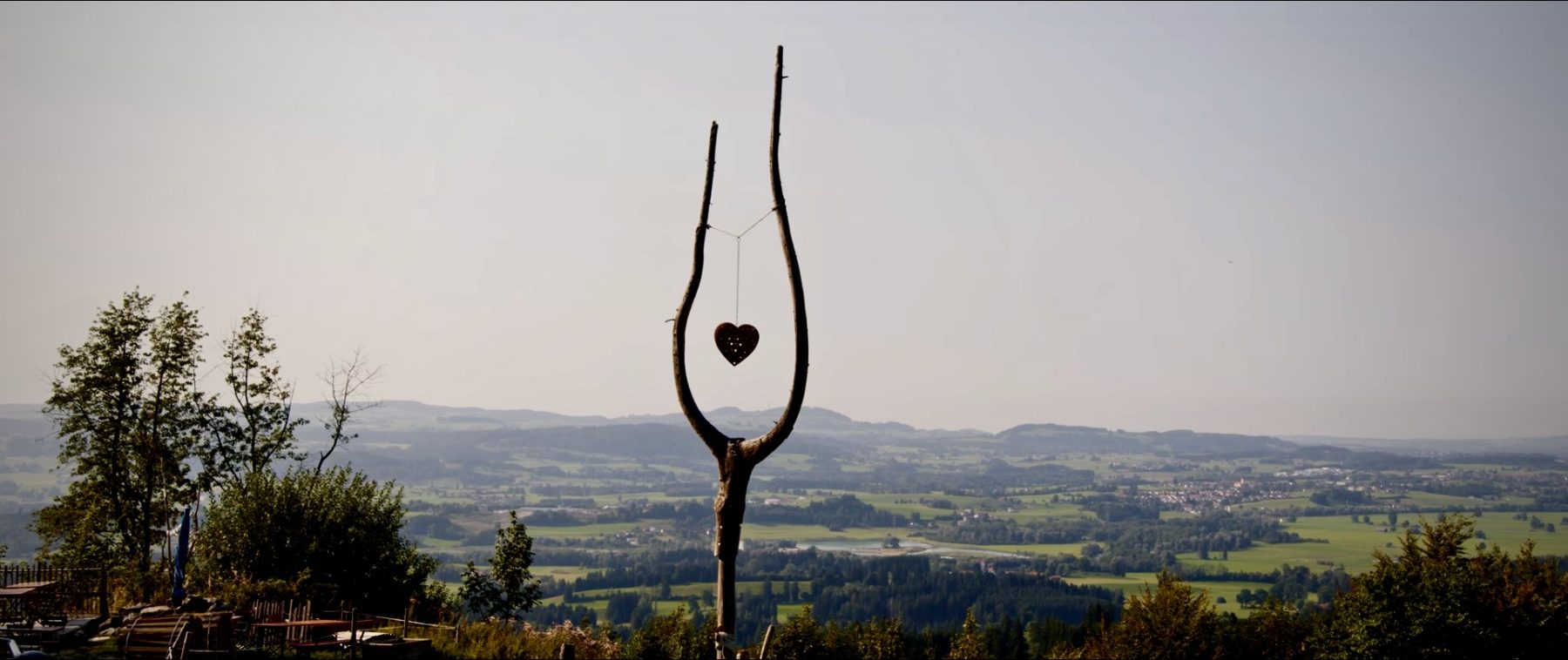 Astgabel mit Herzanhänger vor weitem Ausblick über hügelige Landschaft
