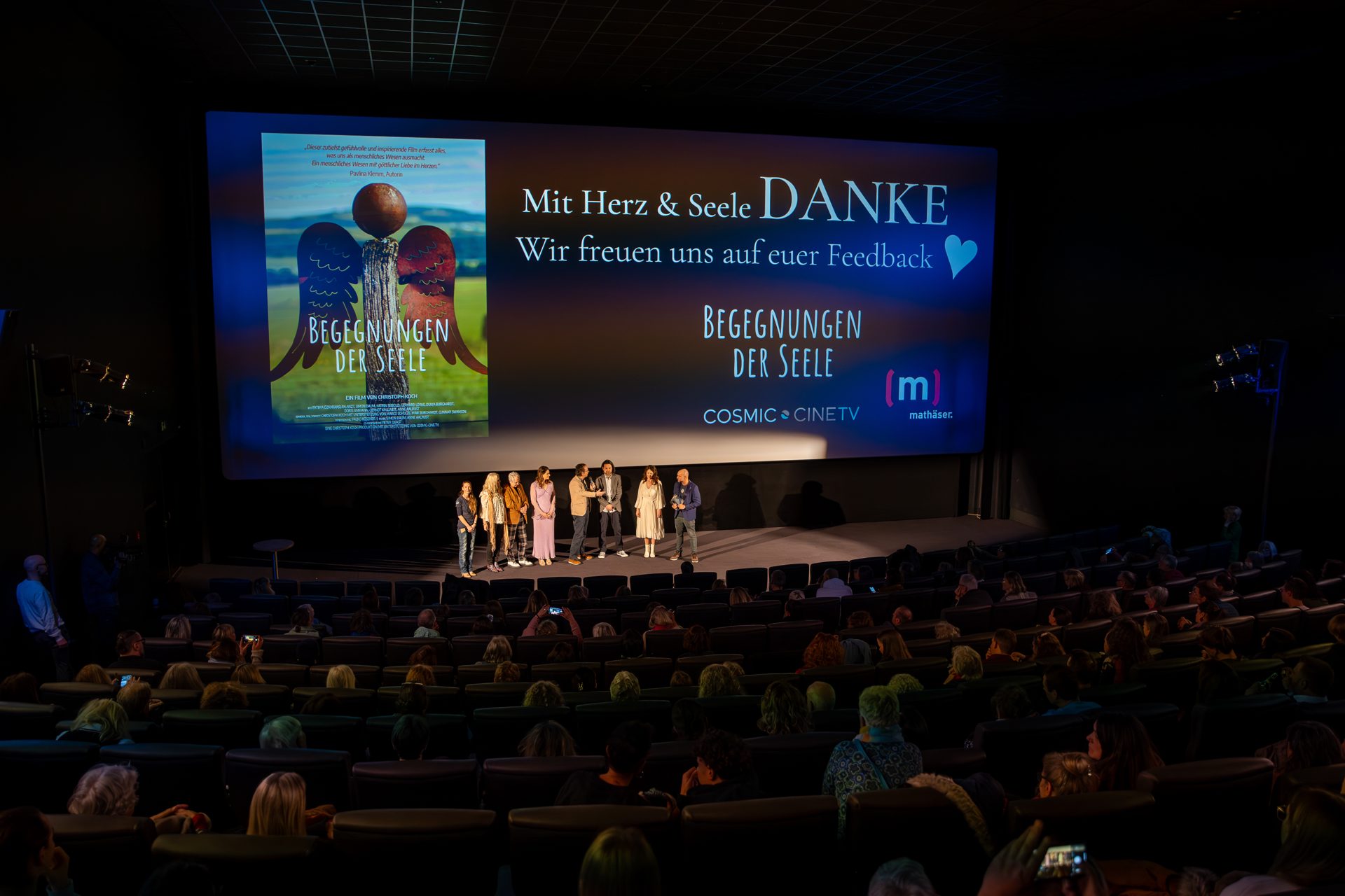 Kinosaal bei der Premiere: Das Team steht auf der Bühne vor der Leinwand mit dem Dank an das Publikum