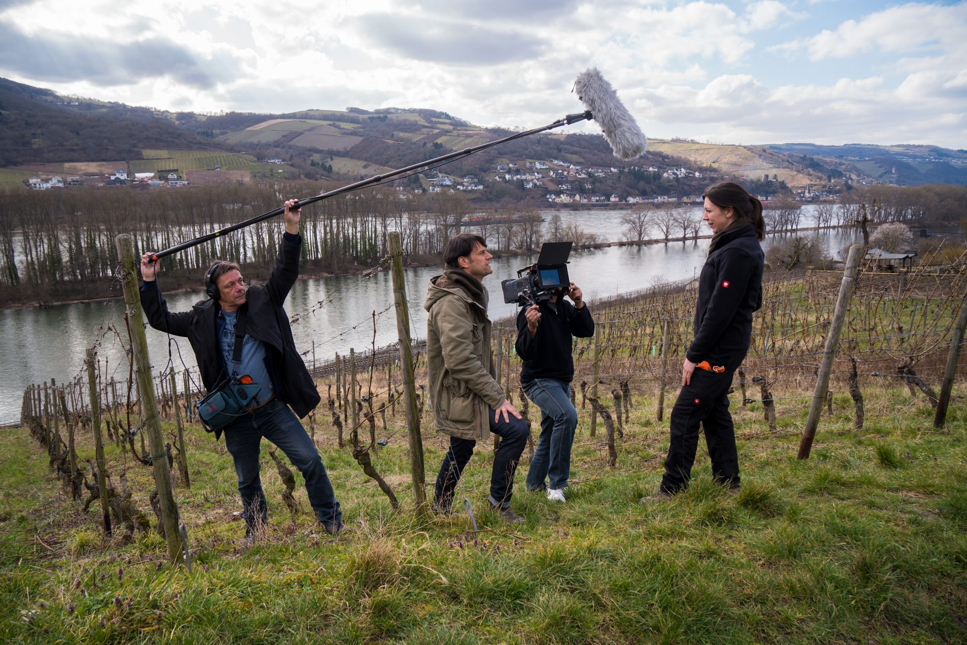 Make-of im Weinberg: Tonangler mit Mikrofon-Galgen, Kameramann und eine Frau über dem Flusstal